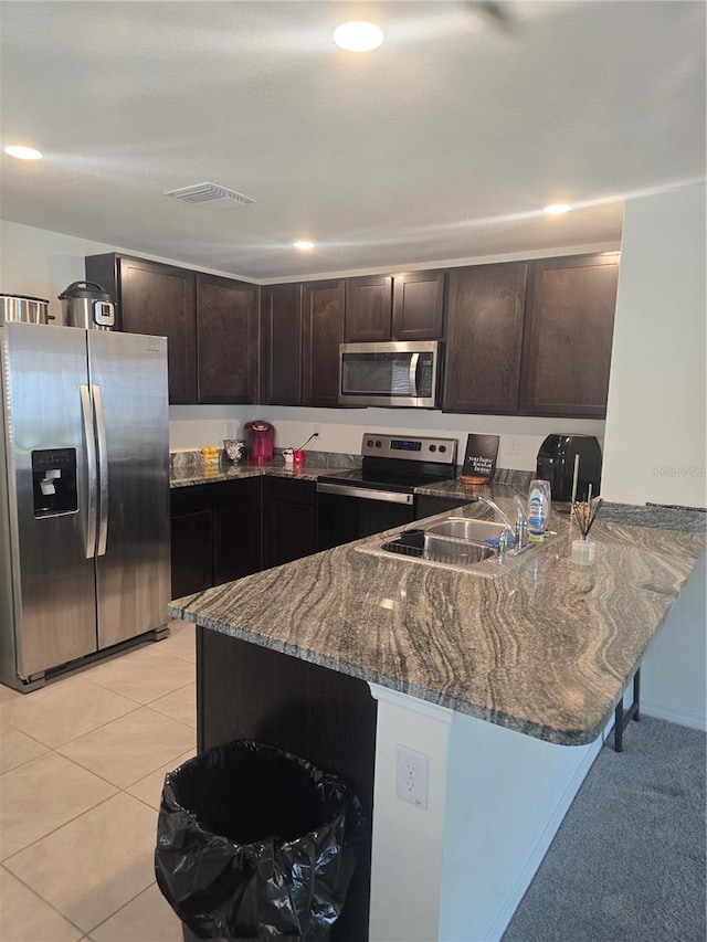 kitchen with dark stone counters, light tile patterned floors, appliances with stainless steel finishes, a peninsula, and a sink