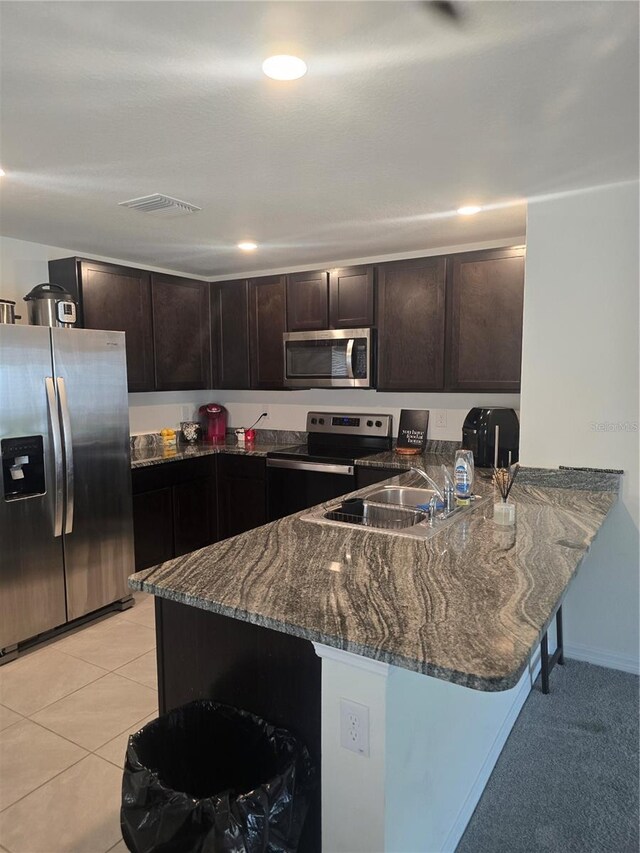 kitchen featuring dark stone countertops, a peninsula, light tile patterned flooring, a sink, and stainless steel appliances
