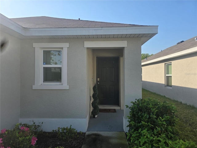 view of exterior entry with stucco siding and a shingled roof