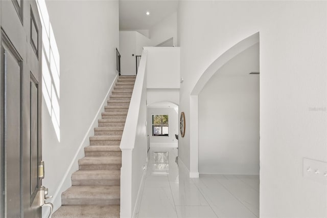 entrance foyer with stairway, baseboards, arched walkways, a towering ceiling, and marble finish floor