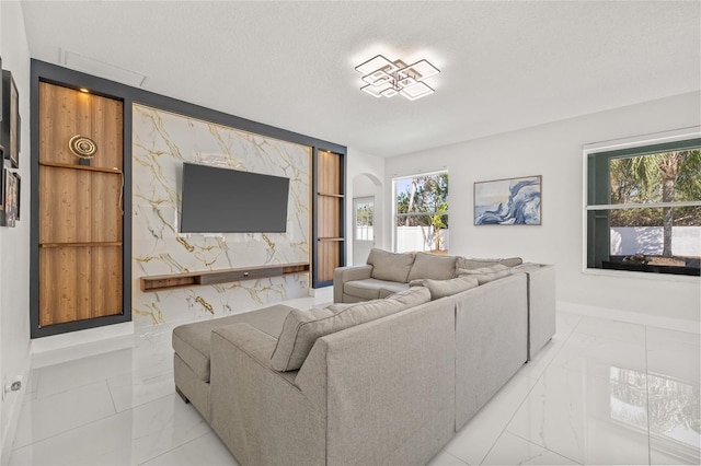 living area with baseboards, arched walkways, a textured ceiling, an accent wall, and marble finish floor