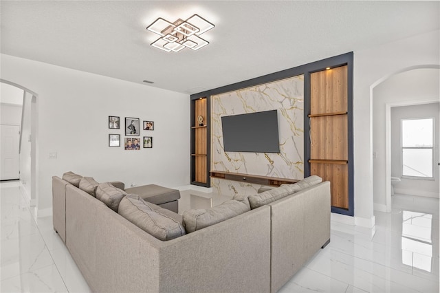 living room with built in shelves, an accent wall, baseboards, arched walkways, and marble finish floor