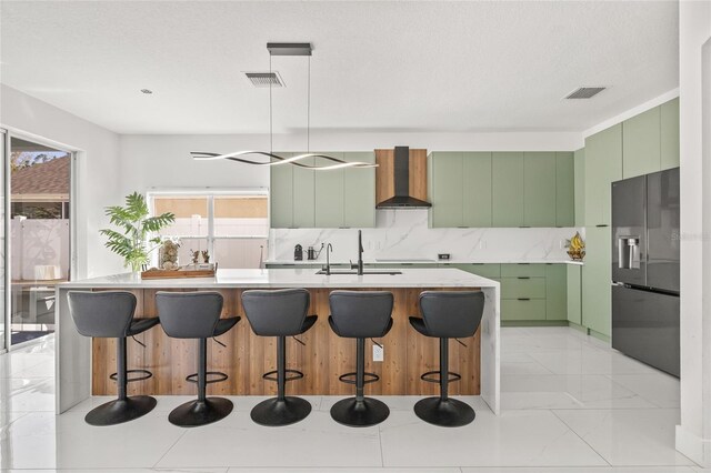 kitchen with visible vents, green cabinets, wall chimney exhaust hood, and stainless steel fridge with ice dispenser