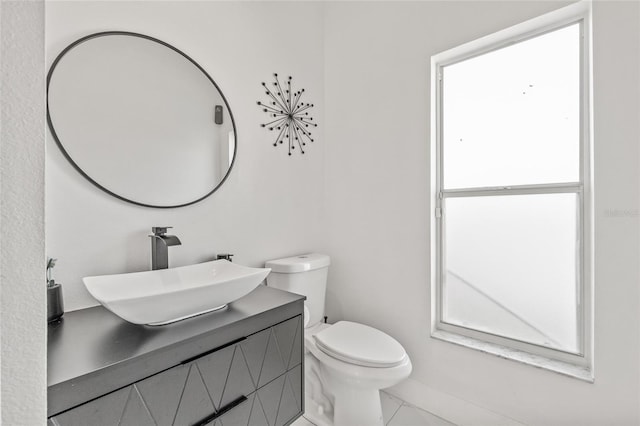 half bath featuring plenty of natural light, toilet, marble finish floor, and vanity