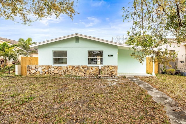 ranch-style home with stucco siding, stone siding, and fence