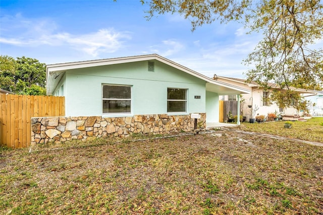 view of property exterior with stucco siding, stone siding, and fence