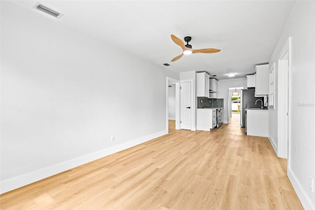 unfurnished living room featuring visible vents, a sink, light wood-style floors, baseboards, and ceiling fan