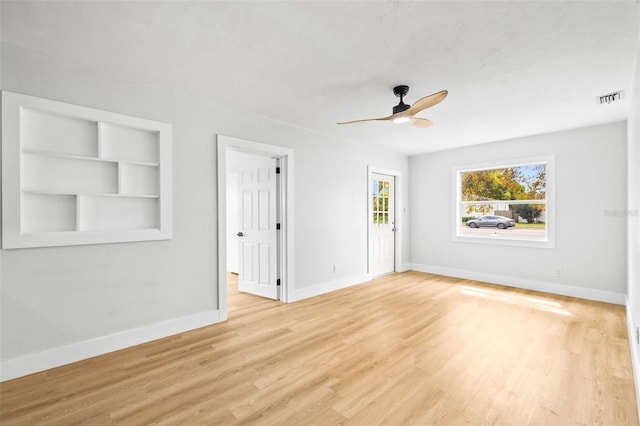 empty room with visible vents, built in shelves, a ceiling fan, wood finished floors, and baseboards