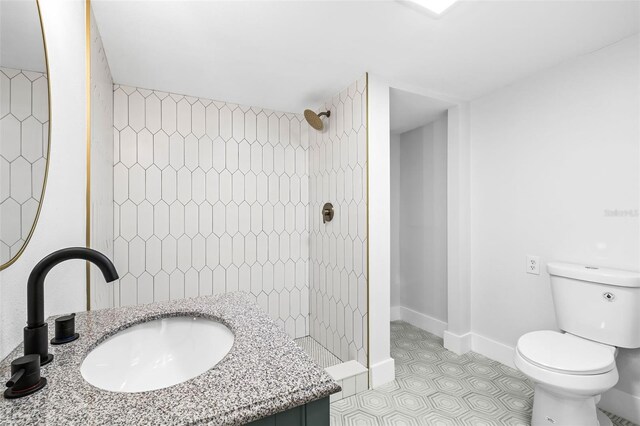 bathroom with toilet, a tile shower, tile patterned flooring, baseboards, and vanity