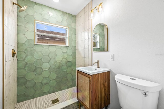 bathroom featuring toilet, tiled shower, and vanity