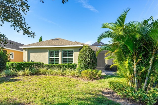 exterior space with stucco siding, a lanai, a front yard, and a shingled roof