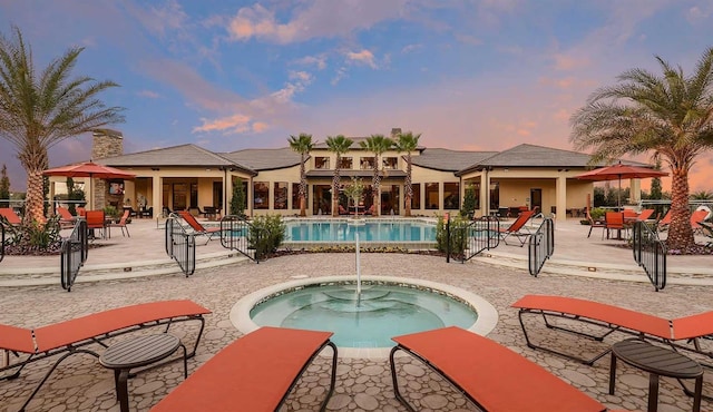 pool at dusk with a patio, a community pool, and a hot tub