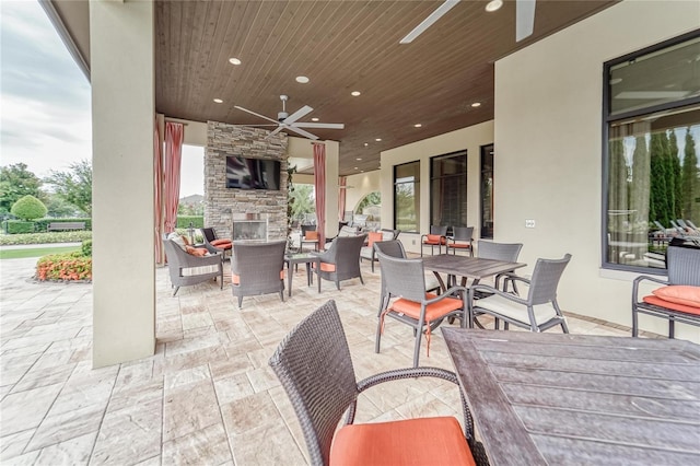 view of patio with outdoor dining area, an outdoor stone fireplace, and ceiling fan