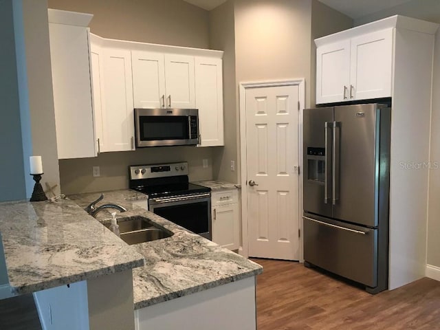 kitchen with light stone countertops, a peninsula, a sink, appliances with stainless steel finishes, and white cabinetry