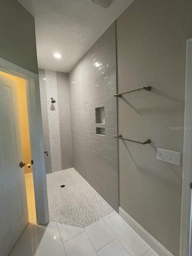 bathroom with baseboards, tiled shower, a textured ceiling, and tile patterned flooring