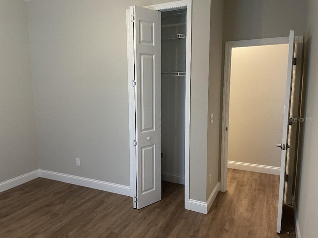 unfurnished bedroom featuring a closet, baseboards, and dark wood-style flooring