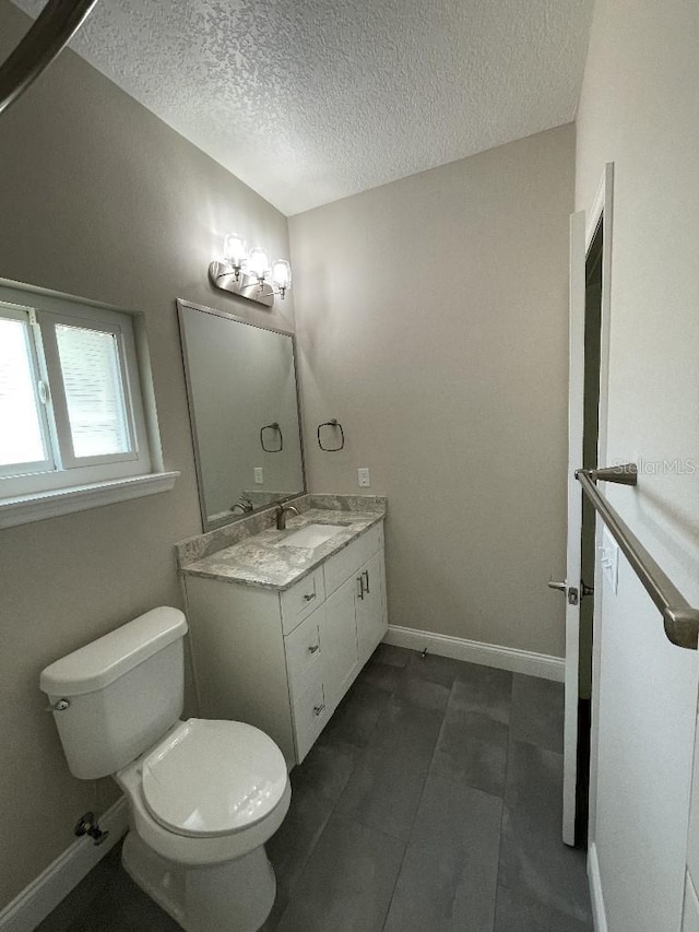 bathroom with baseboards, toilet, vanity, and a textured ceiling