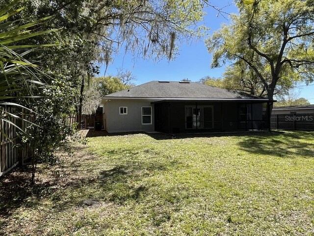 back of house with a lawn, a shingled roof, a fenced backyard, and stucco siding