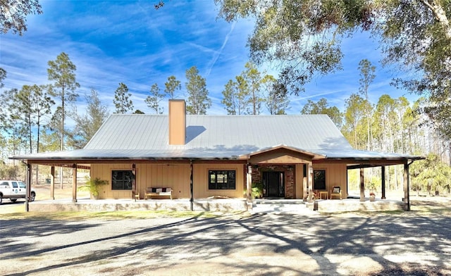 view of front facade featuring a chimney, driveway, metal roof, and a carport