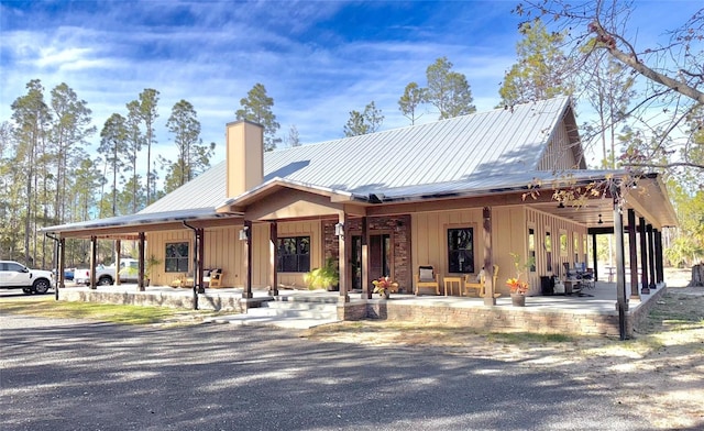 view of front of property featuring a chimney, a porch, metal roof, and board and batten siding