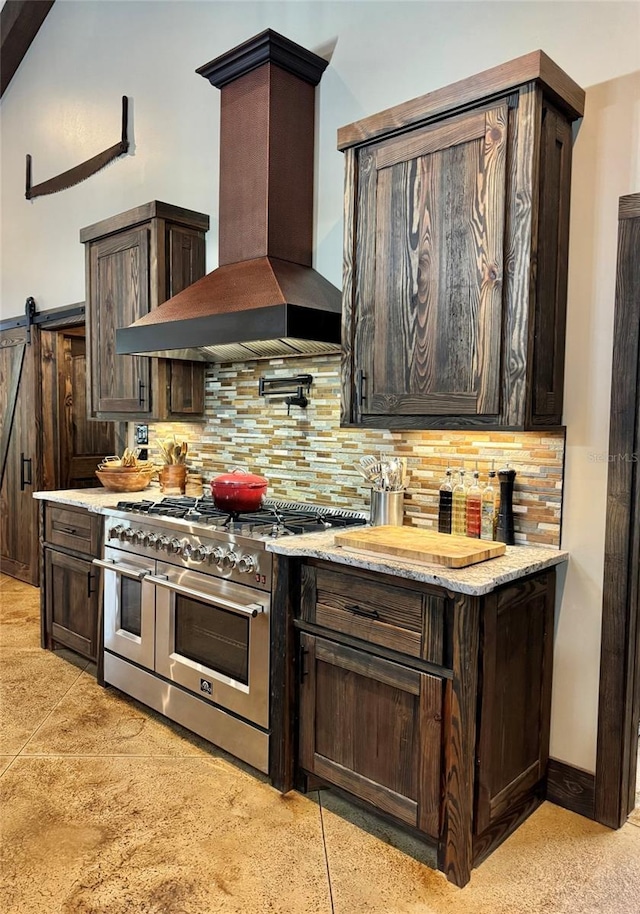 kitchen featuring backsplash, a barn door, wall chimney exhaust hood, range with two ovens, and dark brown cabinets