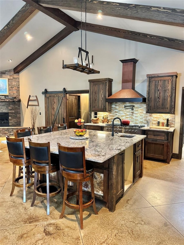 kitchen featuring tasteful backsplash, dark brown cabinetry, beamed ceiling, custom range hood, and a large island with sink