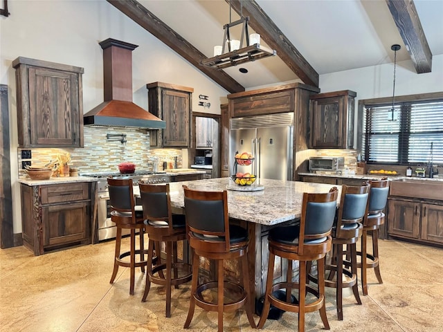 kitchen featuring vaulted ceiling with beams, decorative backsplash, appliances with stainless steel finishes, wall chimney range hood, and a center island