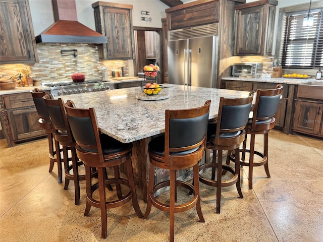 kitchen featuring backsplash, a kitchen island, appliances with stainless steel finishes, light stone countertops, and custom exhaust hood