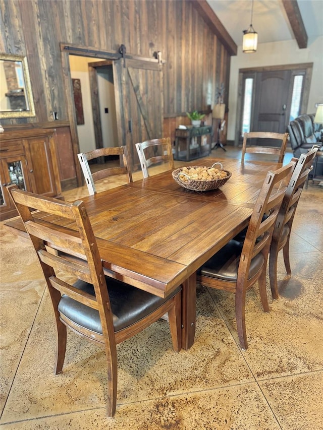 dining area with a barn door, wooden walls, and beam ceiling