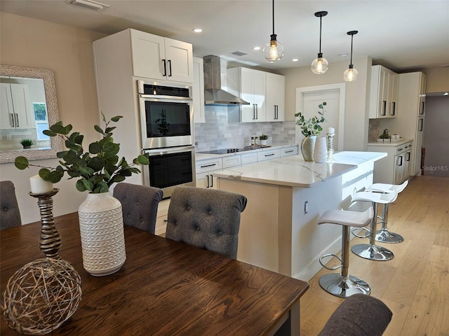 kitchen featuring tasteful backsplash, a kitchen island, light wood-style floors, stainless steel double oven, and wall chimney exhaust hood