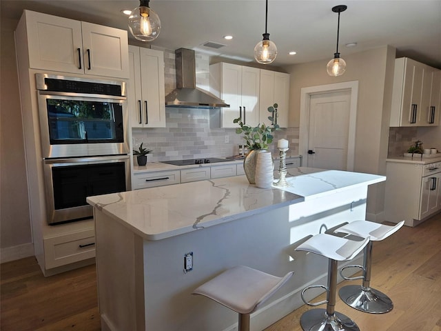 kitchen with wood finished floors, stainless steel double oven, black electric stovetop, decorative backsplash, and wall chimney range hood