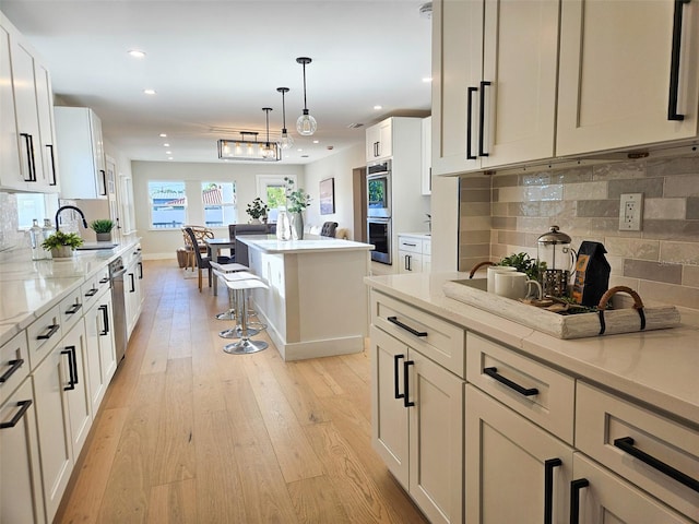 kitchen featuring light stone counters, double oven, light wood-style floors, and a sink