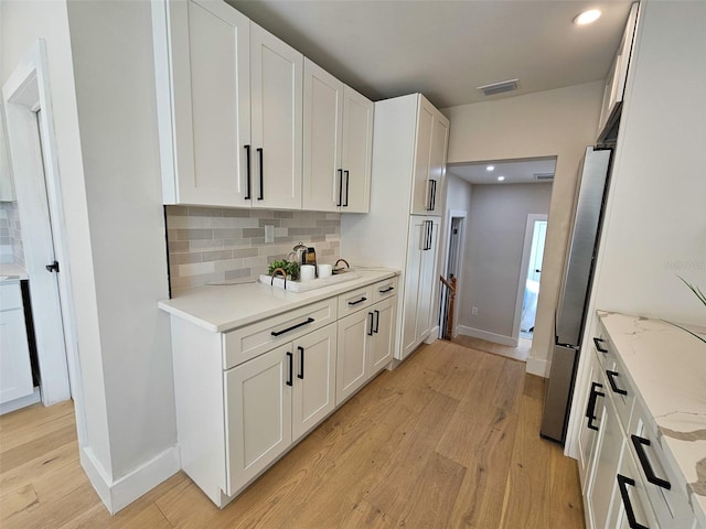 kitchen with visible vents, light wood-style flooring, white cabinetry, freestanding refrigerator, and decorative backsplash