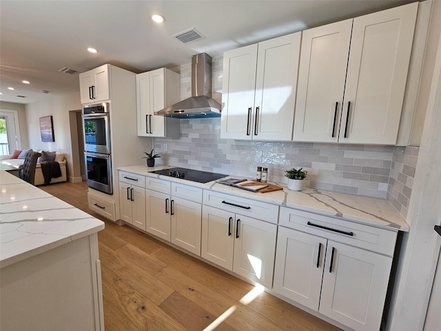 kitchen featuring visible vents, double oven, wall chimney exhaust hood, black electric cooktop, and light wood-type flooring