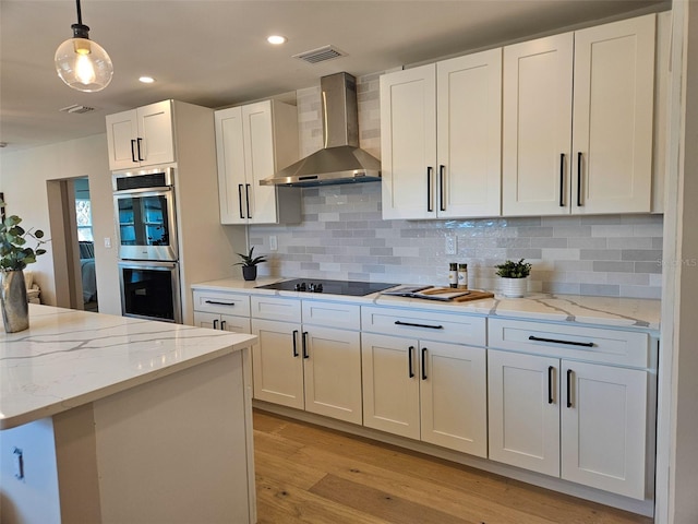 kitchen featuring stainless steel double oven, white cabinetry, black electric stovetop, wall chimney exhaust hood, and light wood-type flooring