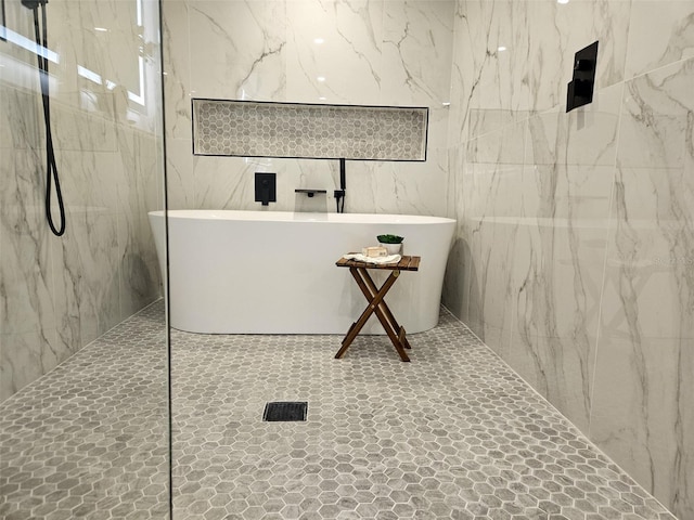 bathroom featuring a marble finish shower, a freestanding bath, and tile walls