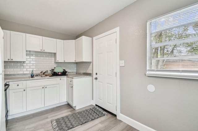 kitchen with light wood-style flooring, backsplash, white cabinetry, light countertops, and baseboards