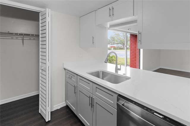 kitchen with a sink, stainless steel dishwasher, dark wood finished floors, light countertops, and baseboards