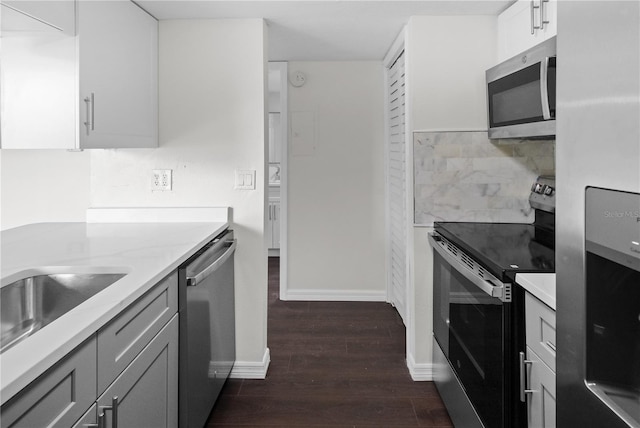 kitchen featuring backsplash, gray cabinetry, light stone countertops, dark wood-style floors, and stainless steel appliances