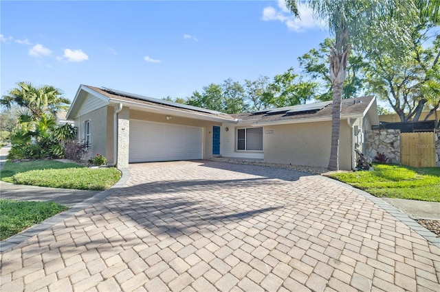 view of front of property with stucco siding, decorative driveway, roof mounted solar panels, fence, and a garage