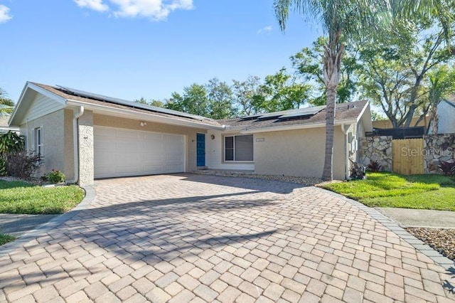 single story home featuring fence, solar panels, stucco siding, a garage, and decorative driveway