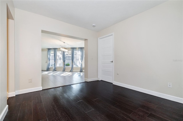 spare room with baseboards, a chandelier, and dark wood-style flooring