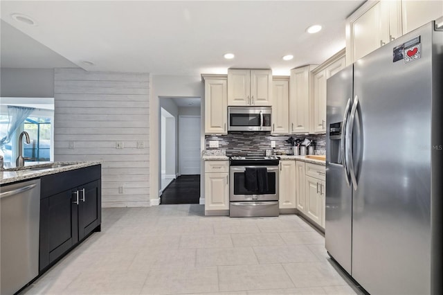 kitchen featuring wooden walls, backsplash, light stone countertops, stainless steel appliances, and a sink