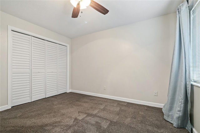 unfurnished bedroom featuring a closet, a ceiling fan, baseboards, and dark colored carpet