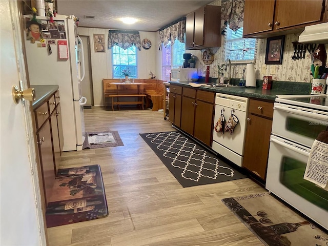 kitchen featuring a sink, white appliances, dark countertops, and light wood finished floors