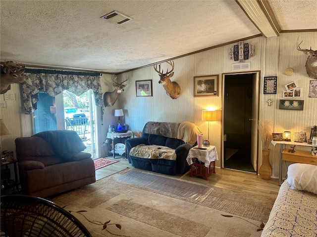 living room featuring visible vents, beamed ceiling, a textured ceiling, light wood-style floors, and crown molding