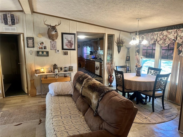 dining area with wallpapered walls, ornamental molding, an inviting chandelier, wood finished floors, and a textured ceiling