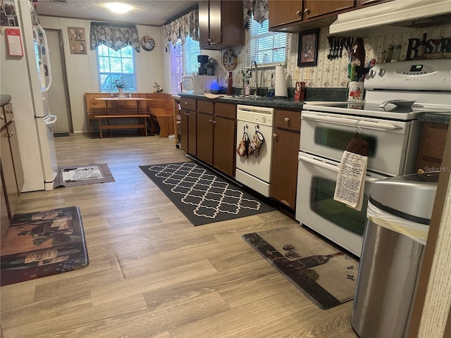 kitchen with light wood-type flooring, under cabinet range hood, a sink, dark countertops, and white appliances