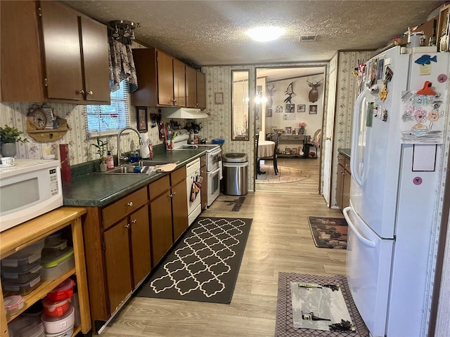 kitchen featuring white appliances, light wood finished floors, wallpapered walls, a sink, and a textured ceiling