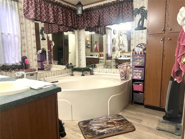 full bathroom with wallpapered walls, wood finished floors, a bath, and vanity